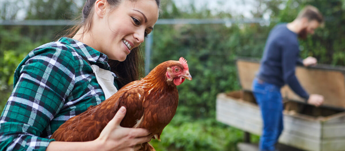 Eine Frau trägt im Garten ein Huhn auf dem Arm