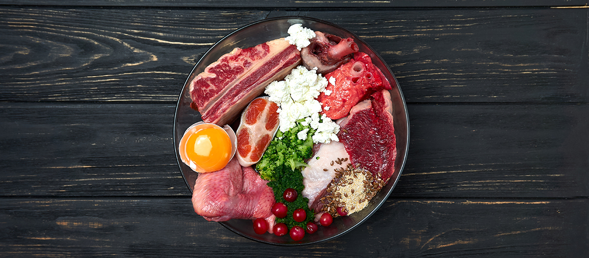Dog food. Natural Organic Raw meat and dairy products, fish, egg, vegetables and supplements. Black wooden background. Close up.