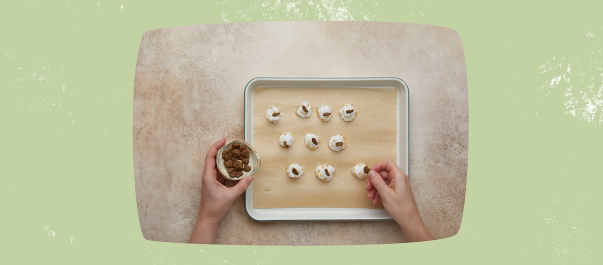 Backblech mit fertigen Baisers, Hände die Leckerlies auf Baisers verteilen Backblech mit fertigen Baisers, Hände die Leckerlies auf Baisers verteilen